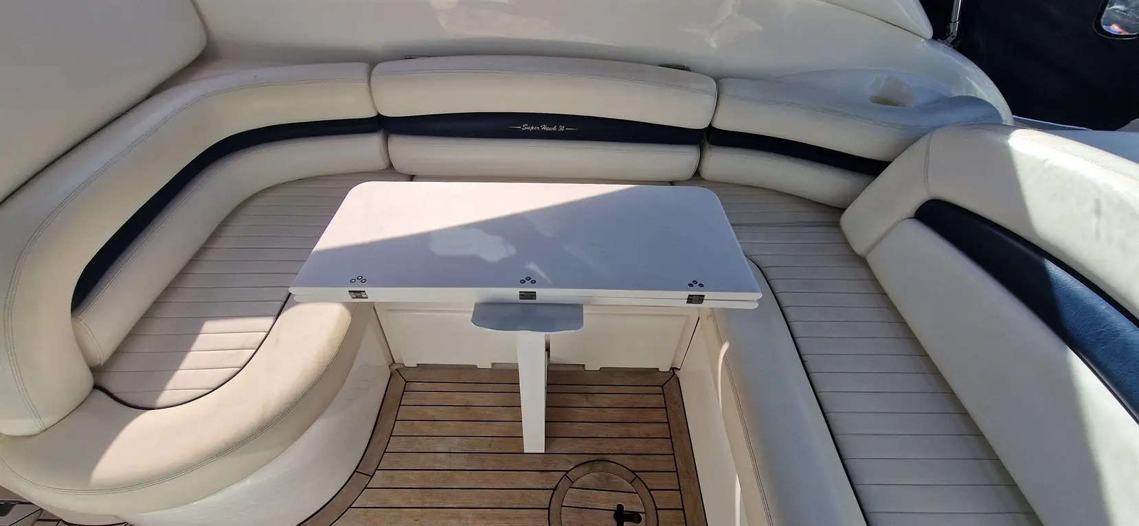 Luxury boat seating area with white leather cushions and a foldable table on polished wooden flooring.